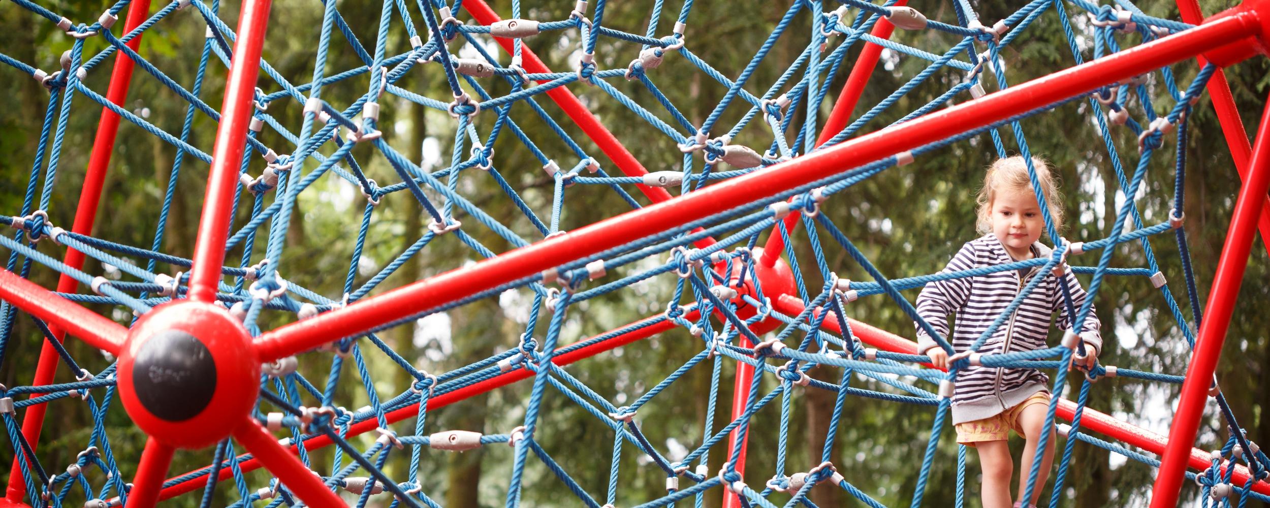 Ein Kind kletter auf einem Spielgerät aus Seilen, das aussieht wie ein Netz