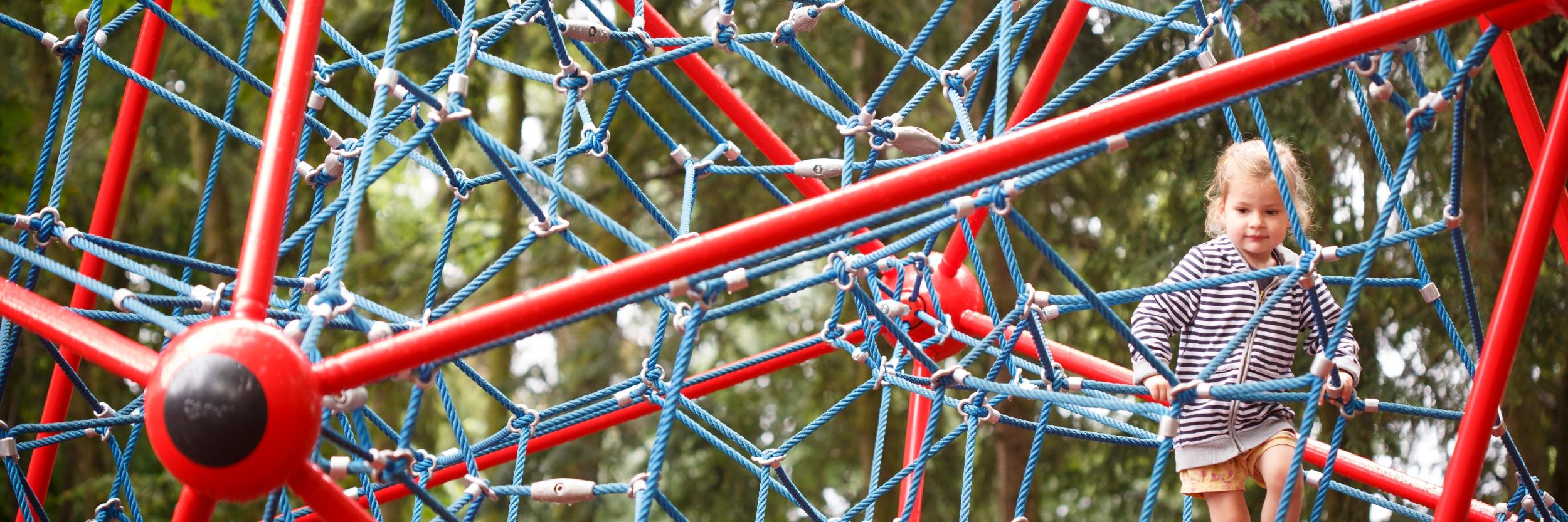 Ein Kind kletter auf einem Spielgerät aus Seilen, das aussieht wie ein Netz