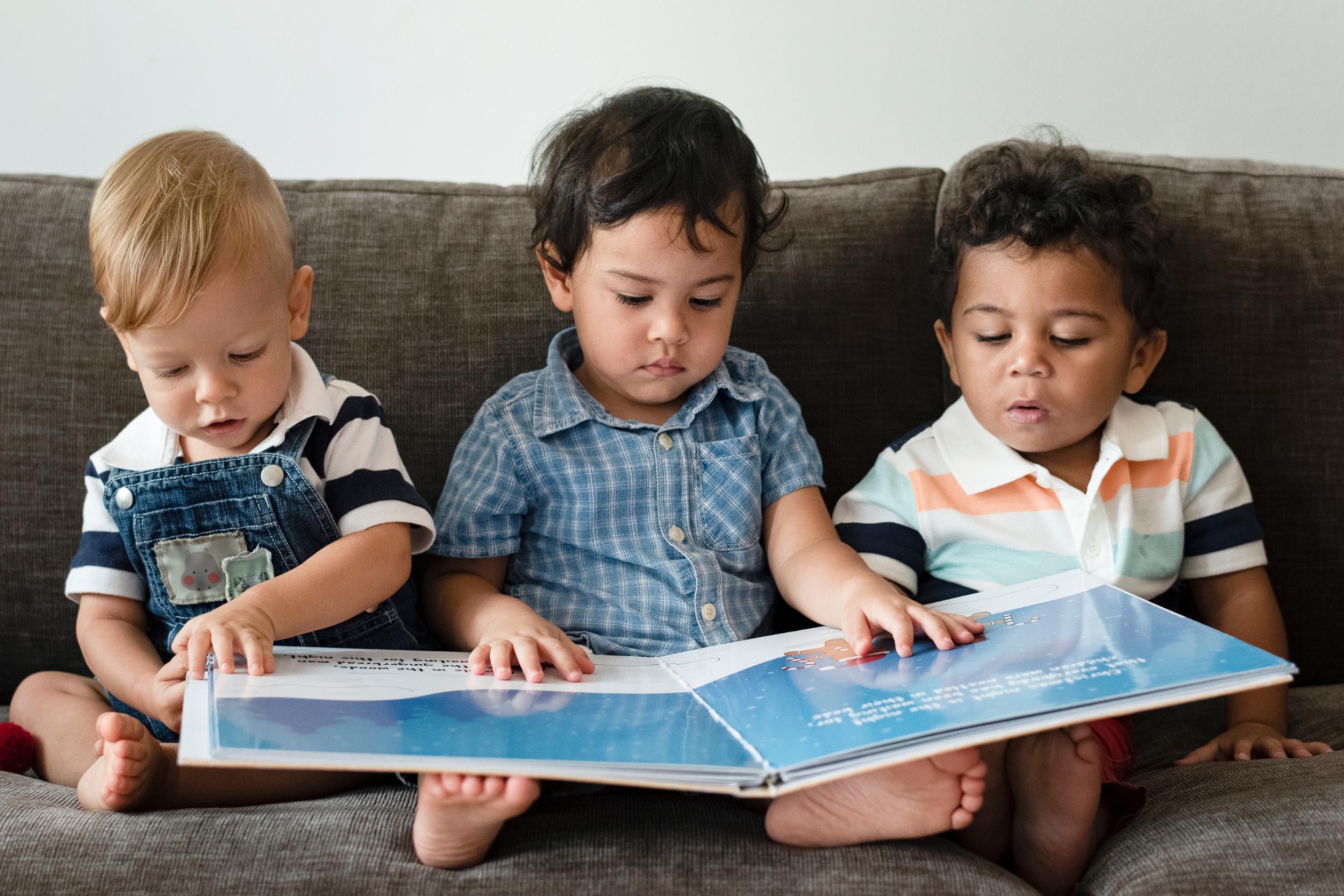 drei kleine Kinder sitzen auf dem Sofa und schauen ein Bilderbuch an