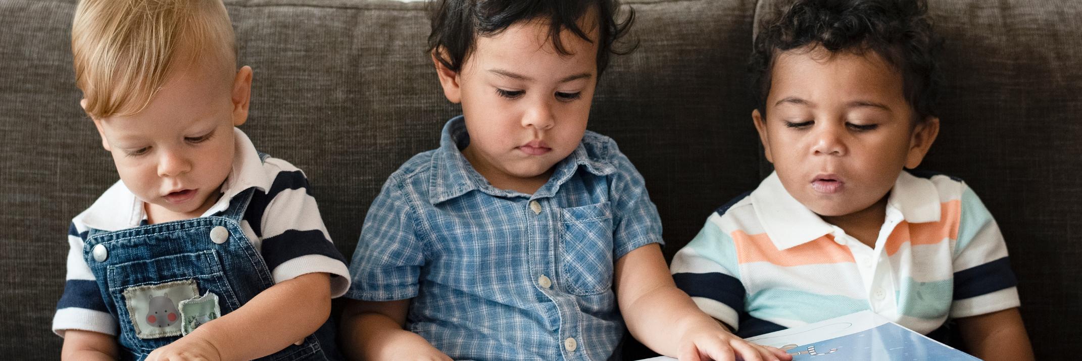 drei kleine Kinder sitzen auf dem Sofa und schauen ein Bilderbuch an