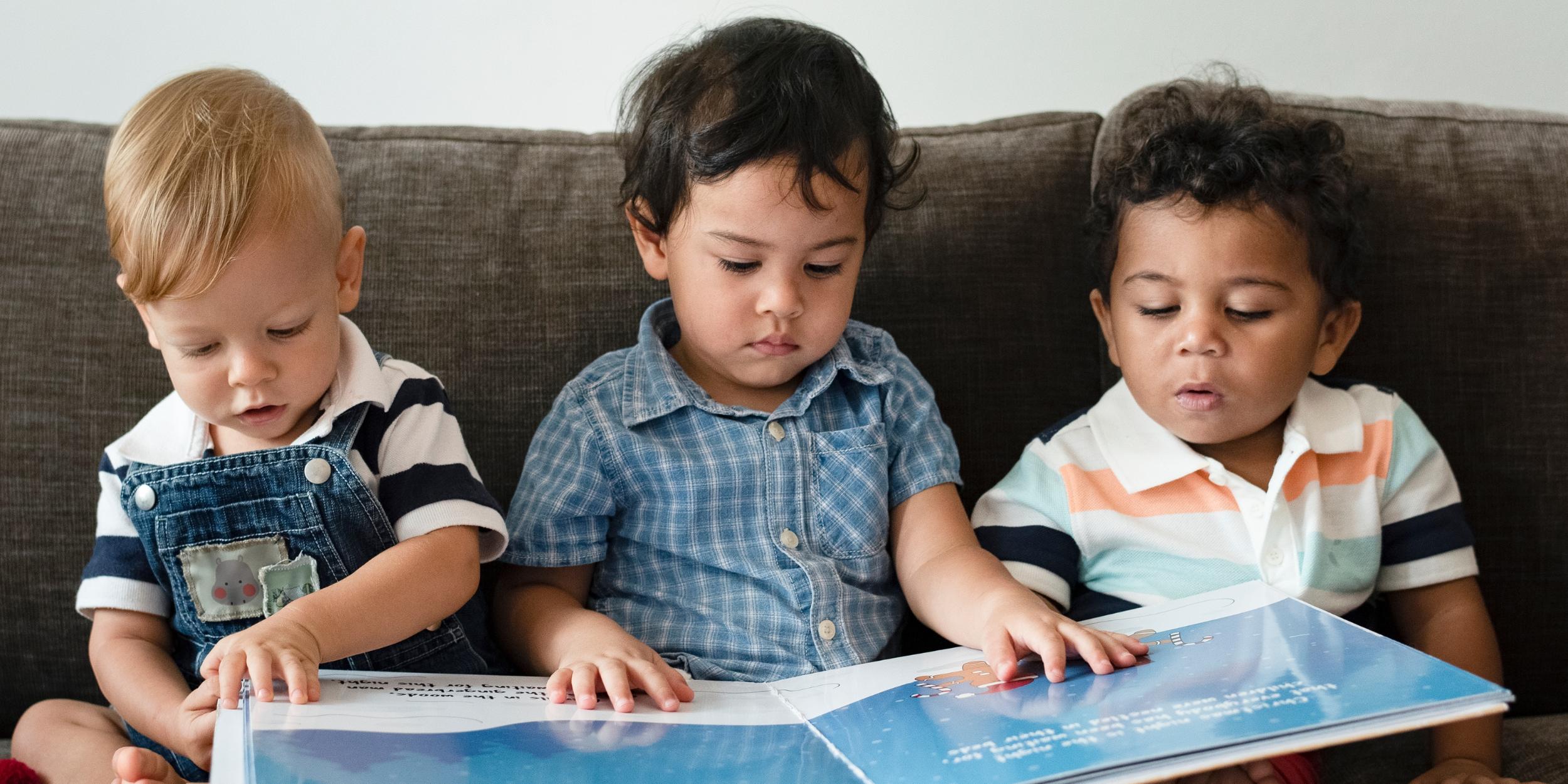 drei kleine Kinder sitzen auf dem Sofa und schauen ein Bilderbuch an