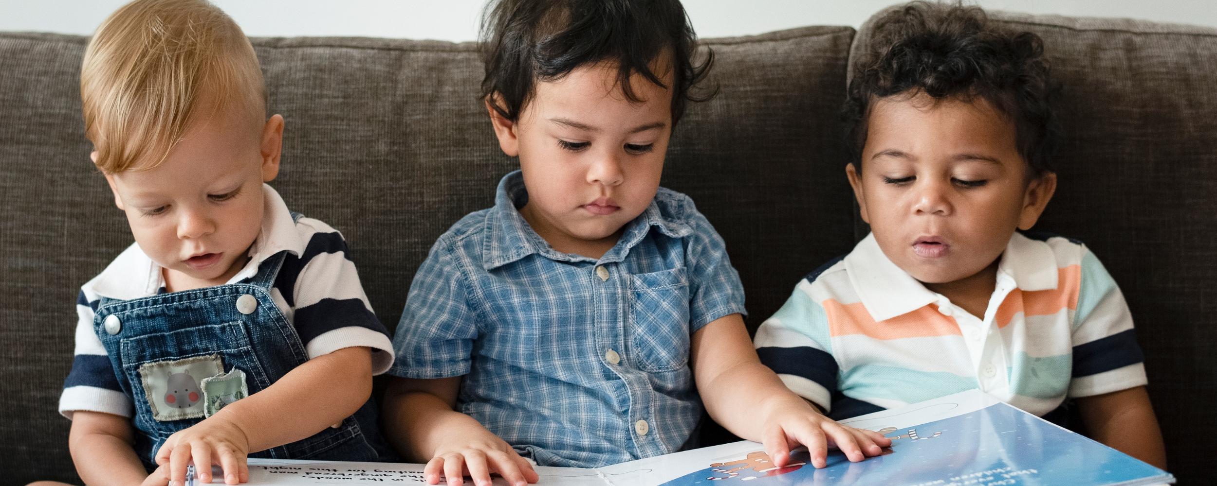 drei kleine Kinder sitzen auf dem Sofa und schauen ein Bilderbuch an