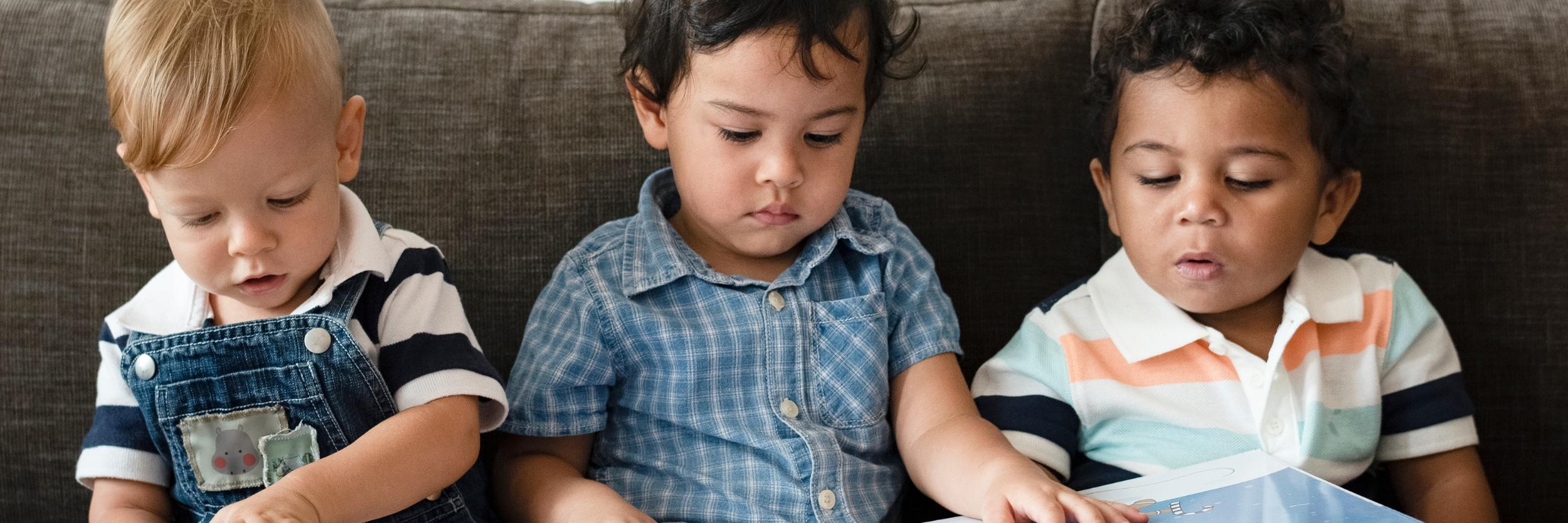 drei kleine Kinder sitzen auf dem Sofa und schauen ein Bilderbuch an