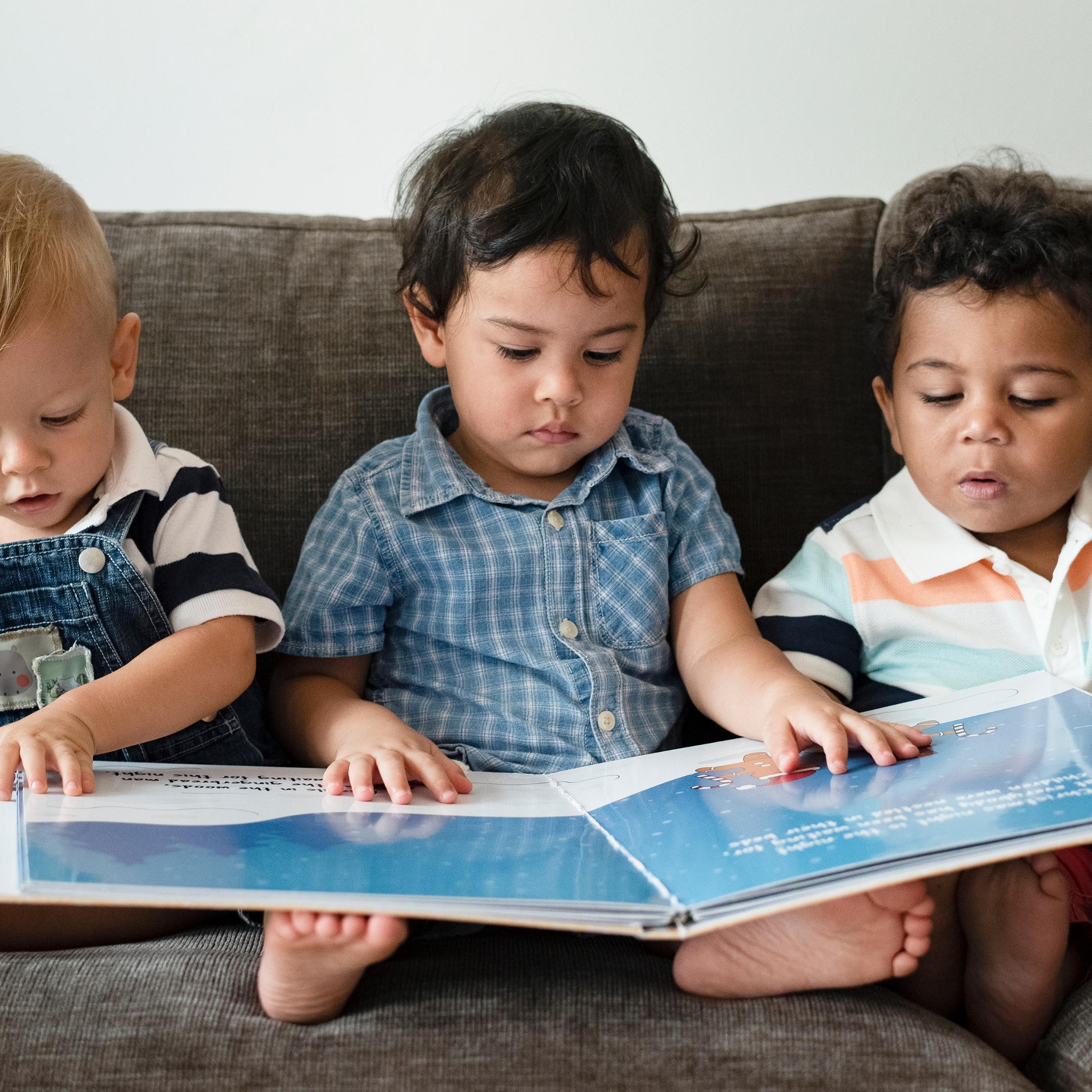 drei kleine Kinder sitzen auf dem Sofa und schauen ein Bilderbuch an
