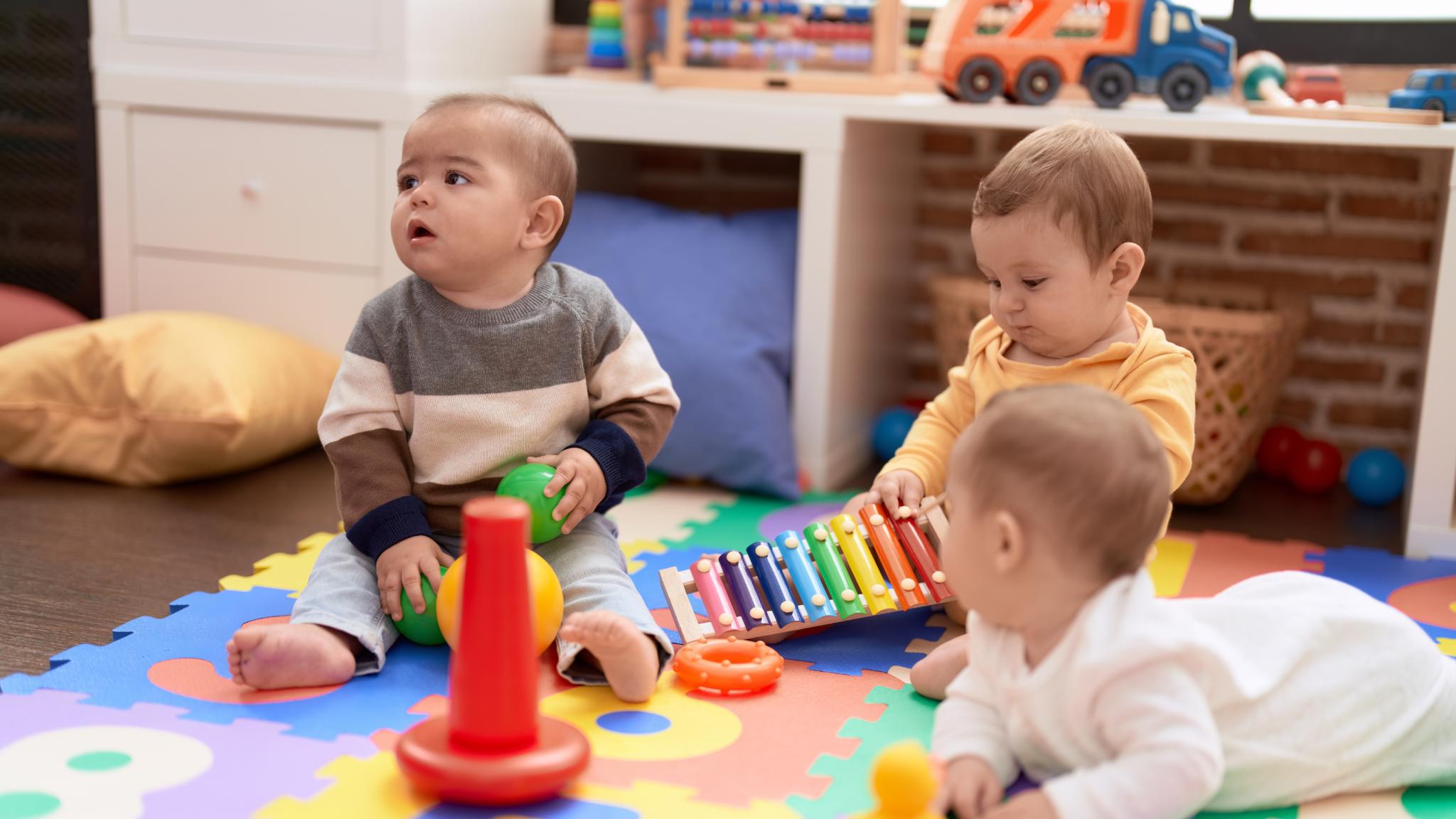 Drei Babys sitzen auf dem Boden und spielen mit Spielzeug
