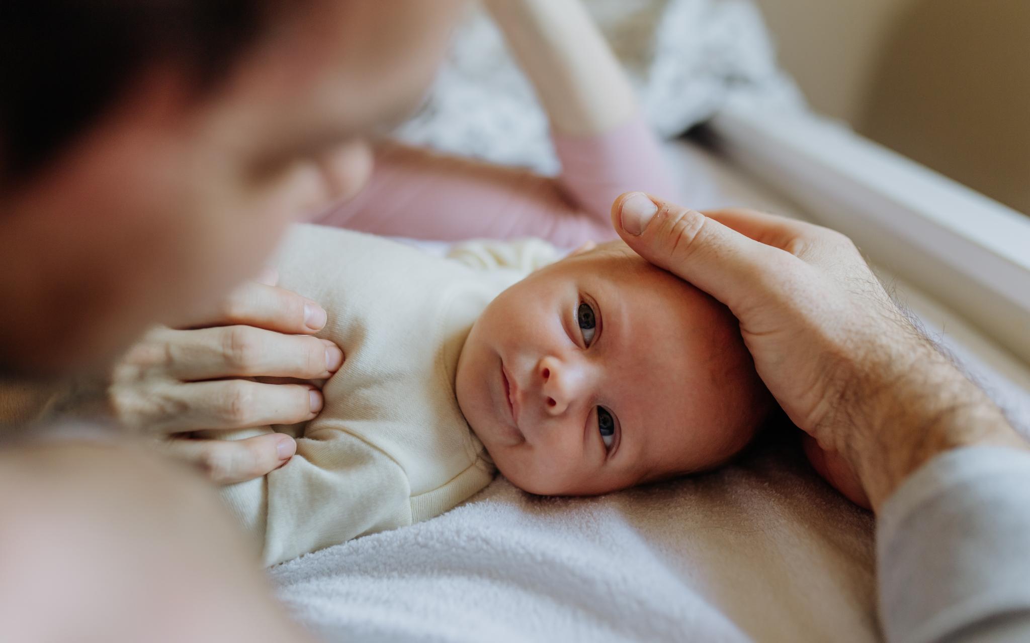 Ein Baby liegt auf dem Rücken. Ein Vater hält zärtlich den Kopf. (c) Shutterstock Ein Baby liegt auf dem Rücken. Ein Vater hält zärtlich den Kopf.