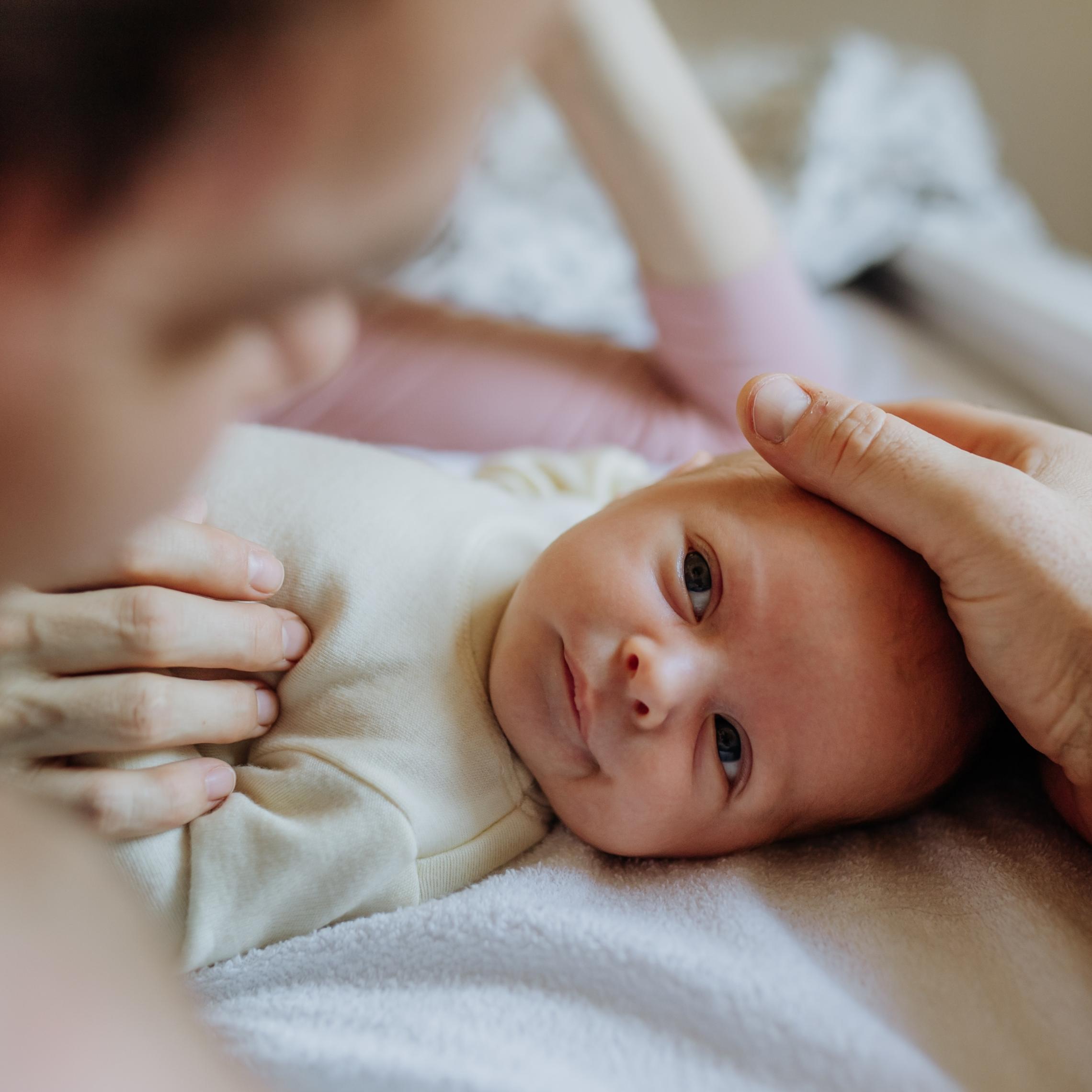 Ein Baby liegt auf dem Rücken. Ein Vater hält zärtlich den Kopf.