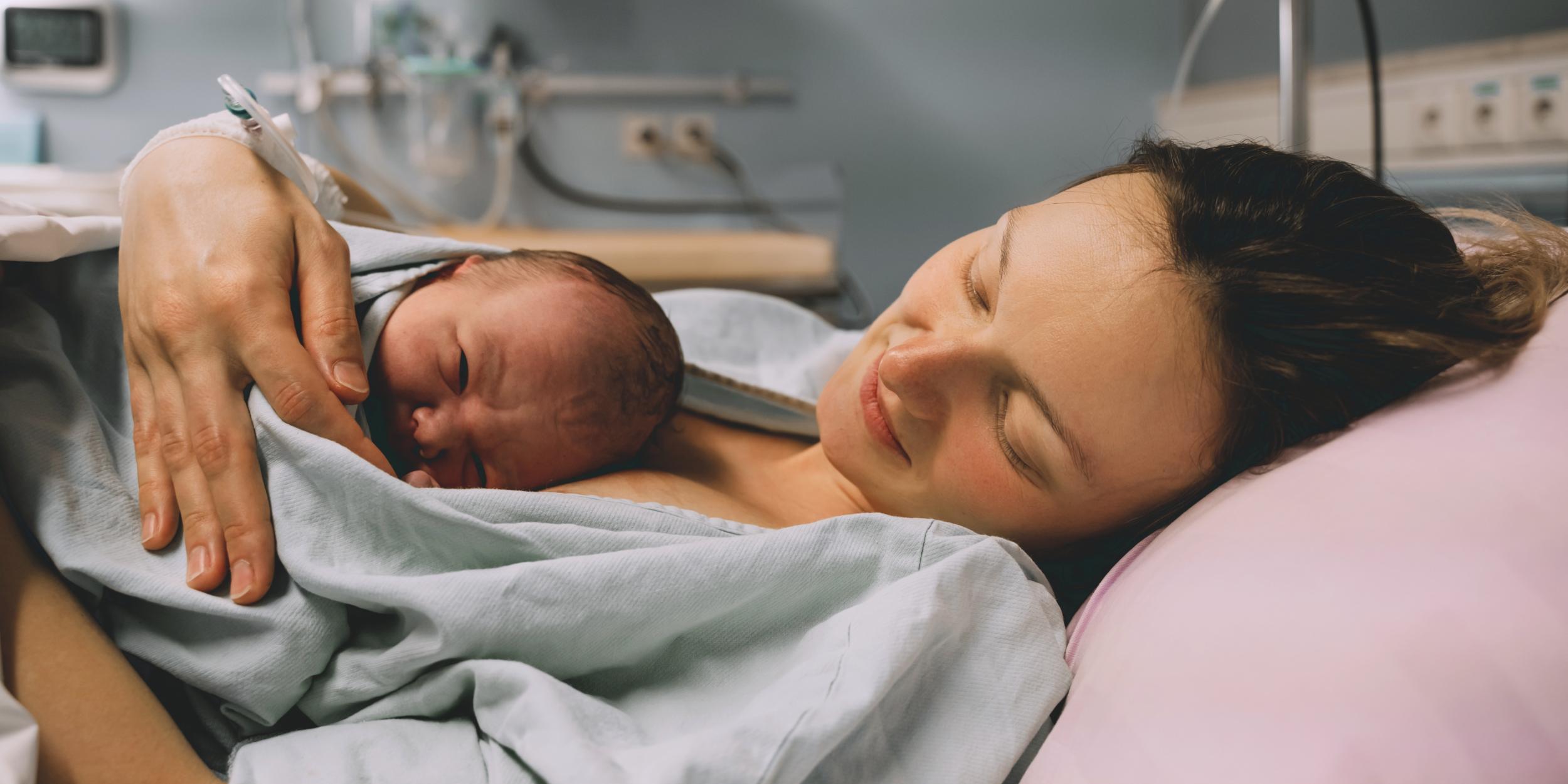 Mutter liegt im Bett mit neugeborenem Baby kurz nach der Geburt