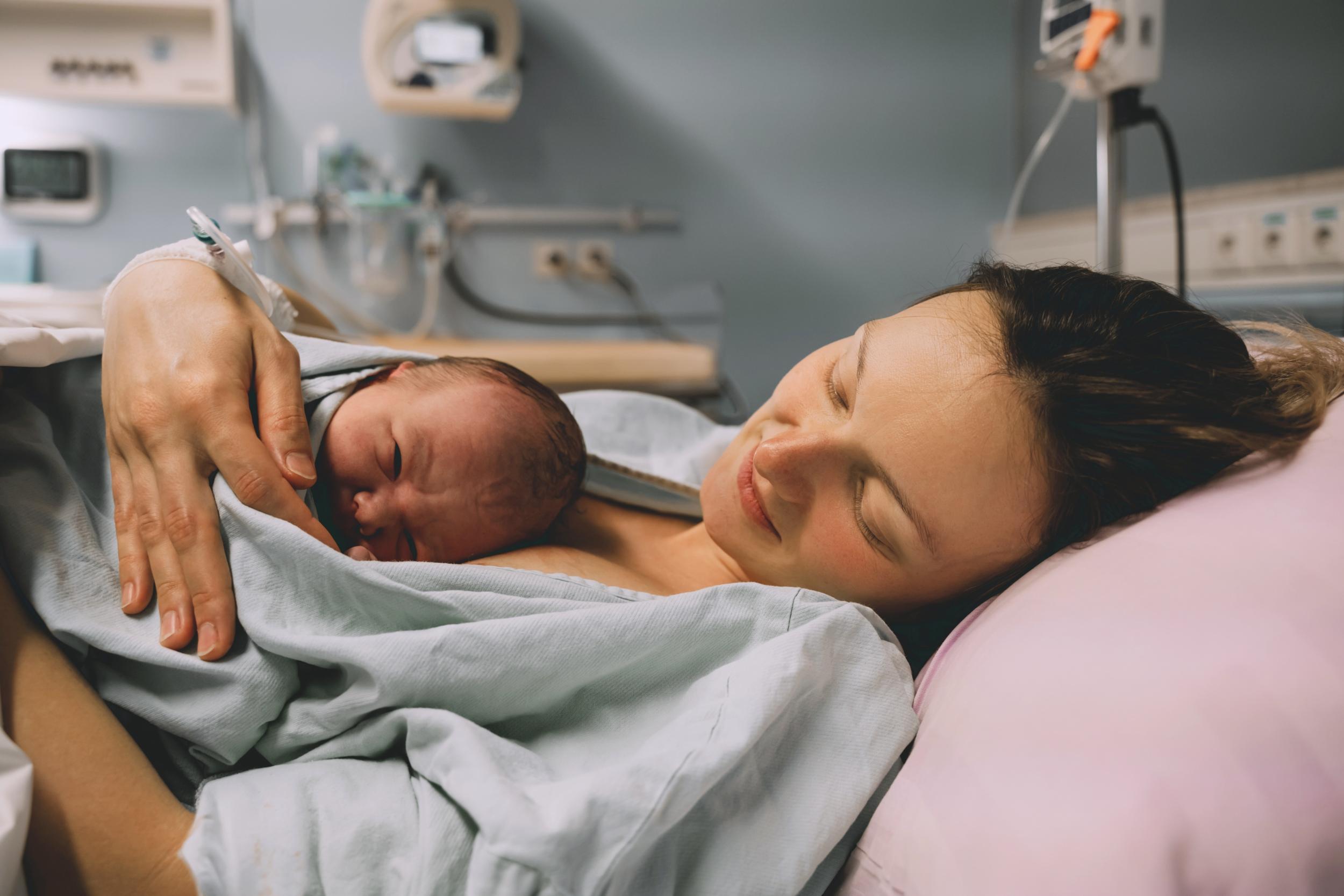 Mutter liegt im Bett mit neugeborenem Baby kurz nach der Geburt