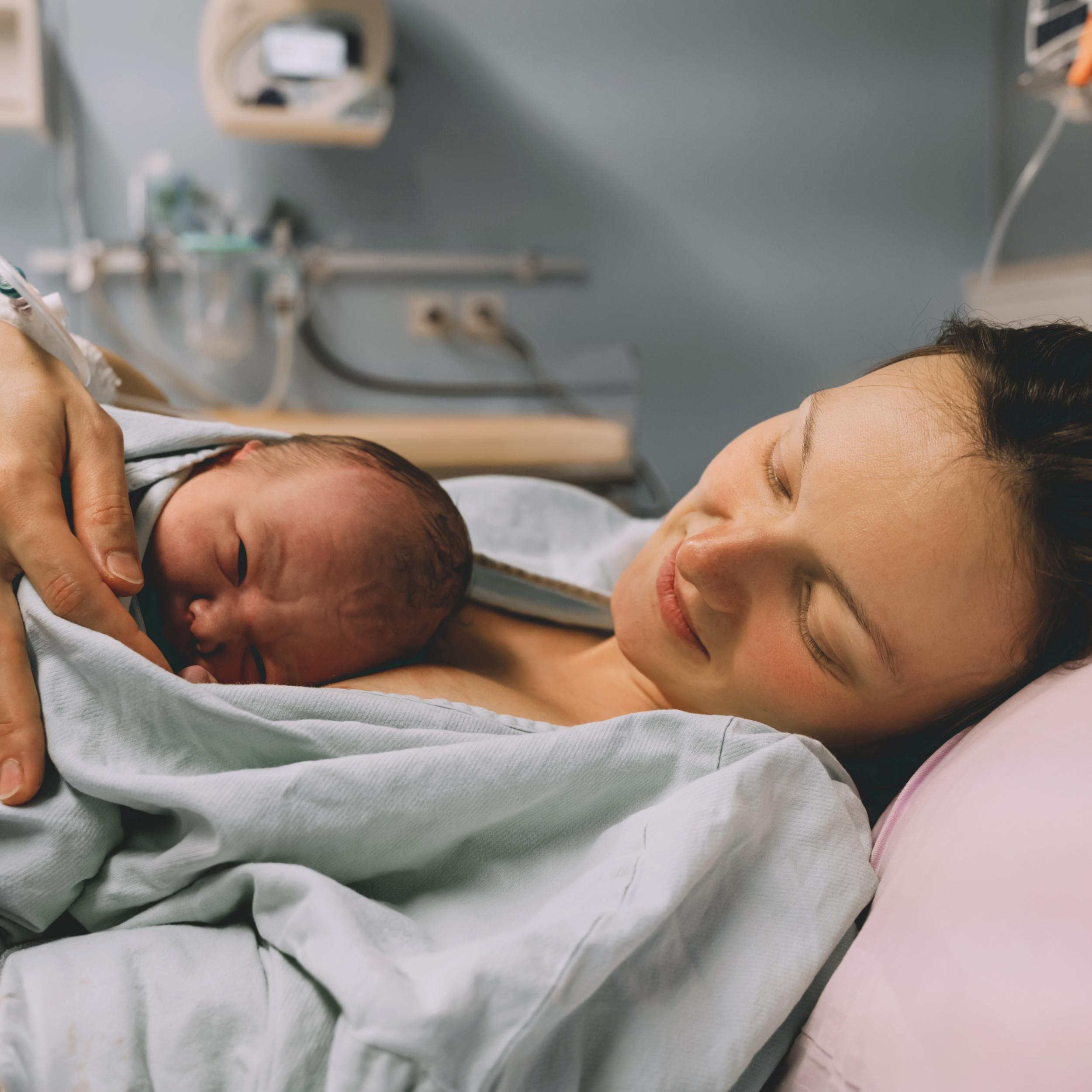 Mutter liegt im Bett mit neugeborenem Baby kurz nach der Geburt