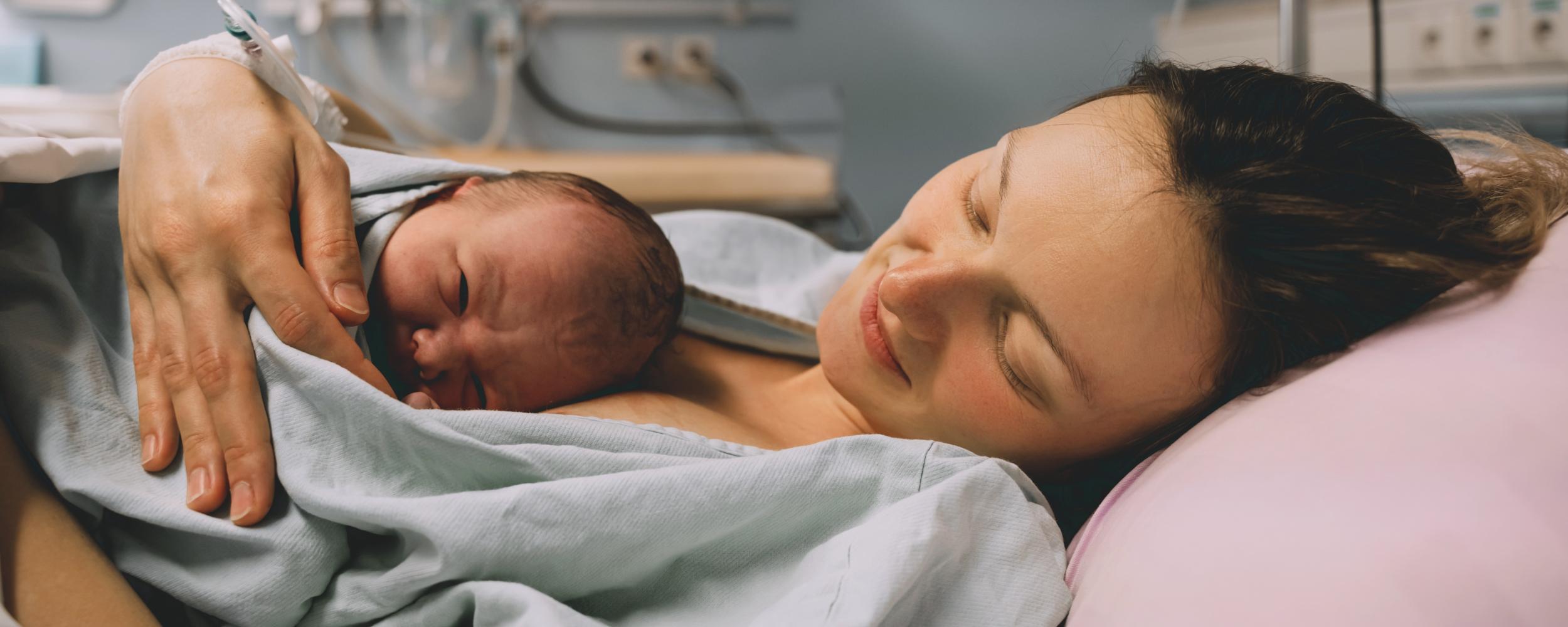 Mutter liegt im Bett mit neugeborenem Baby kurz nach der Geburt