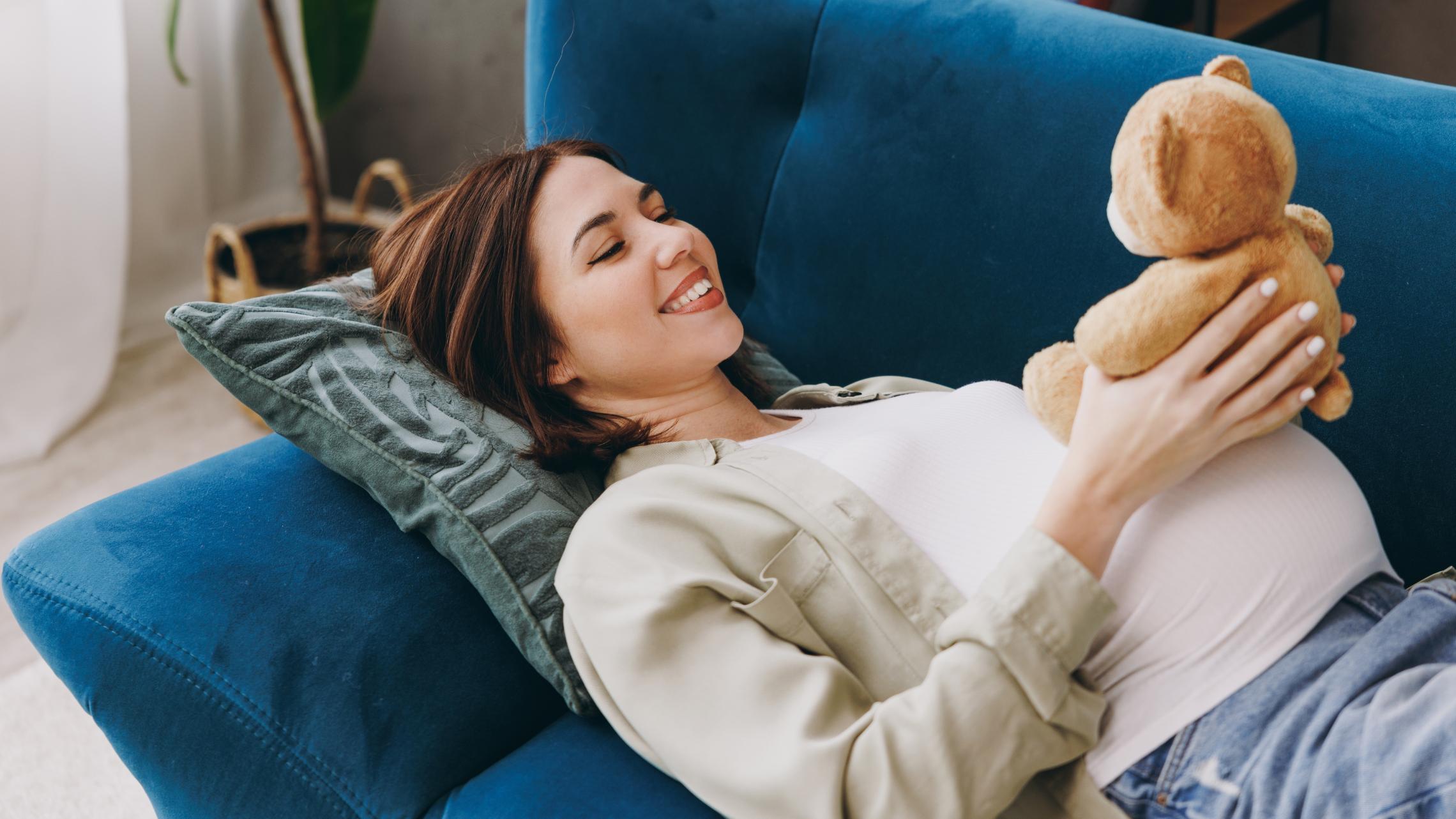 Frau liegt auf einem blauen Sofa und hält einen Teddybär in den Händen