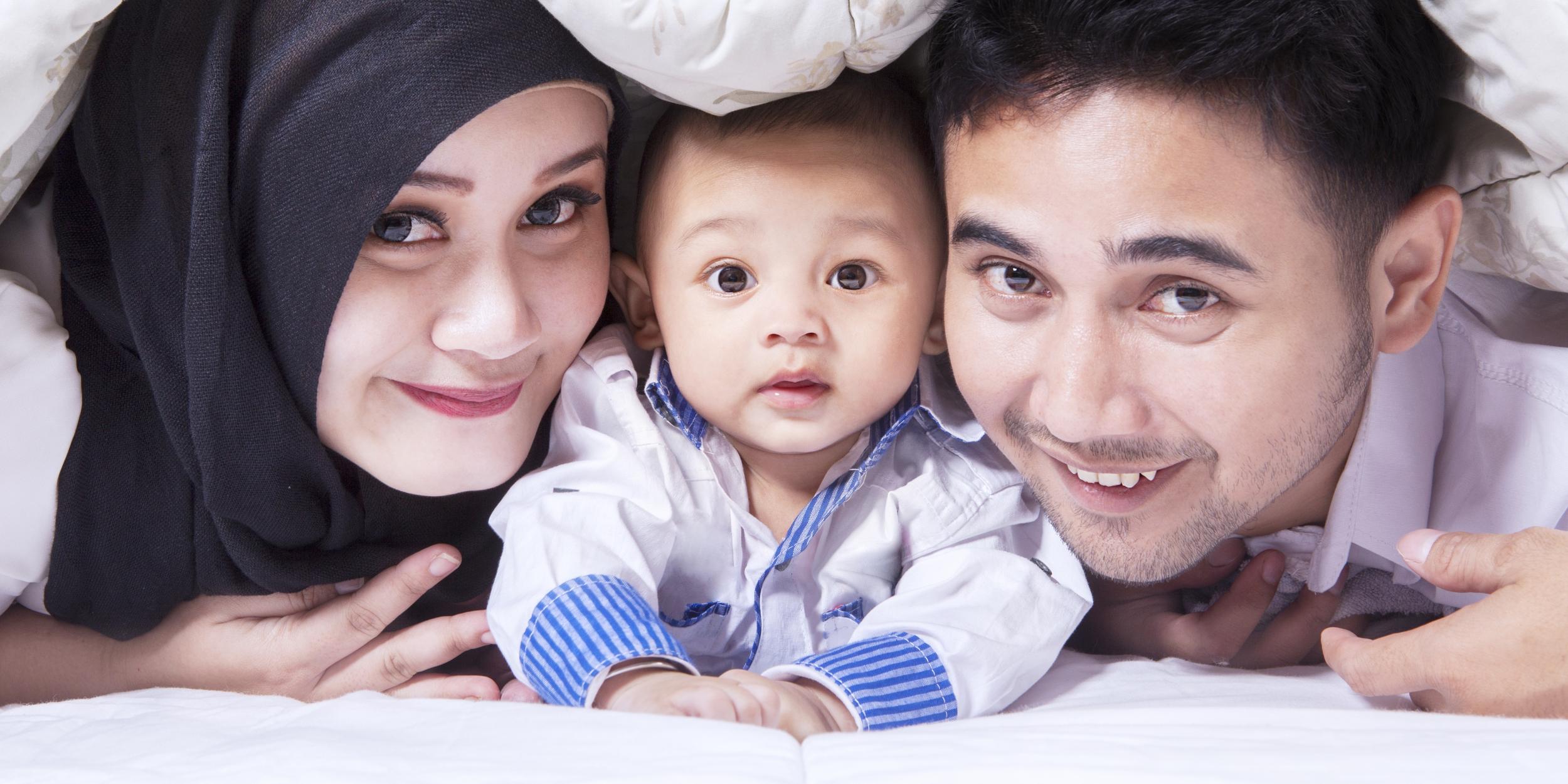 Familienbild mit einer jungen Mutter mit Kopftuch, einem Baby in der Mitte und einem Vater