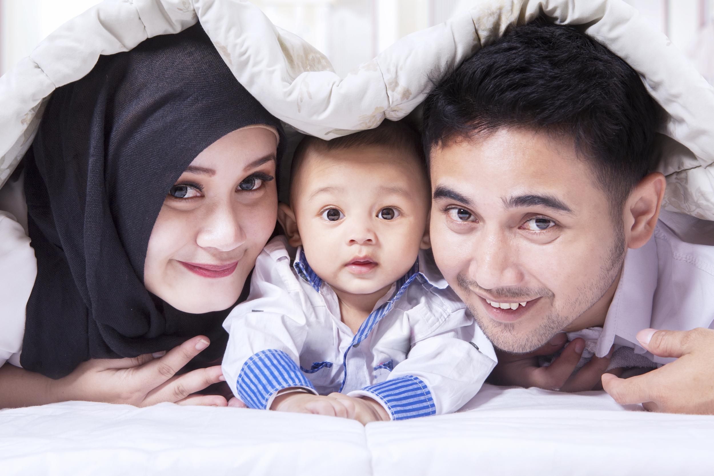 Familienbild mit einer jungen Mutter mit Kopftuch, einem Baby in der Mitte und einem Vater