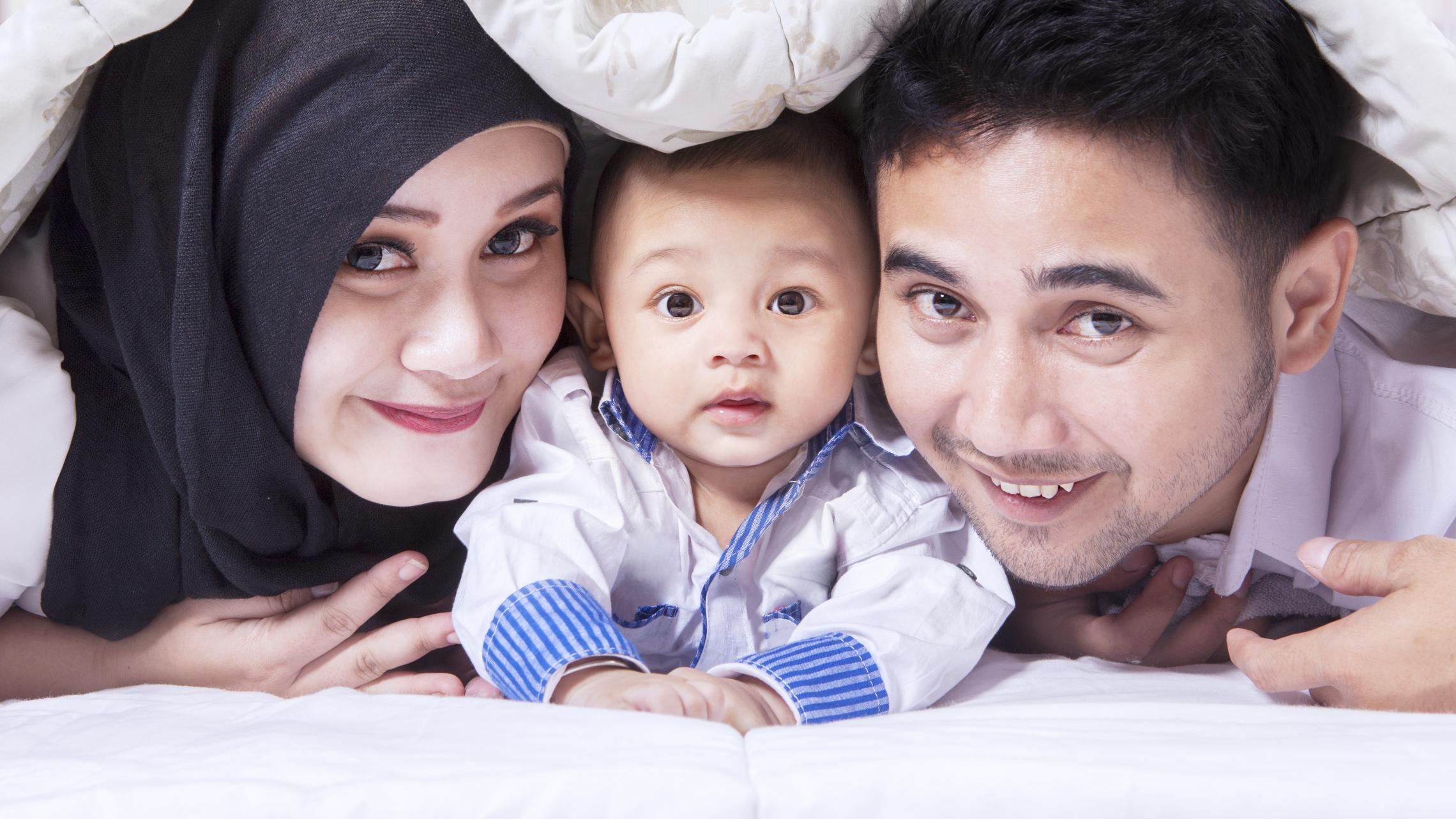 Familienbild mit einer jungen Mutter mit Kopftuch, einem Baby in der Mitte und einem Vater