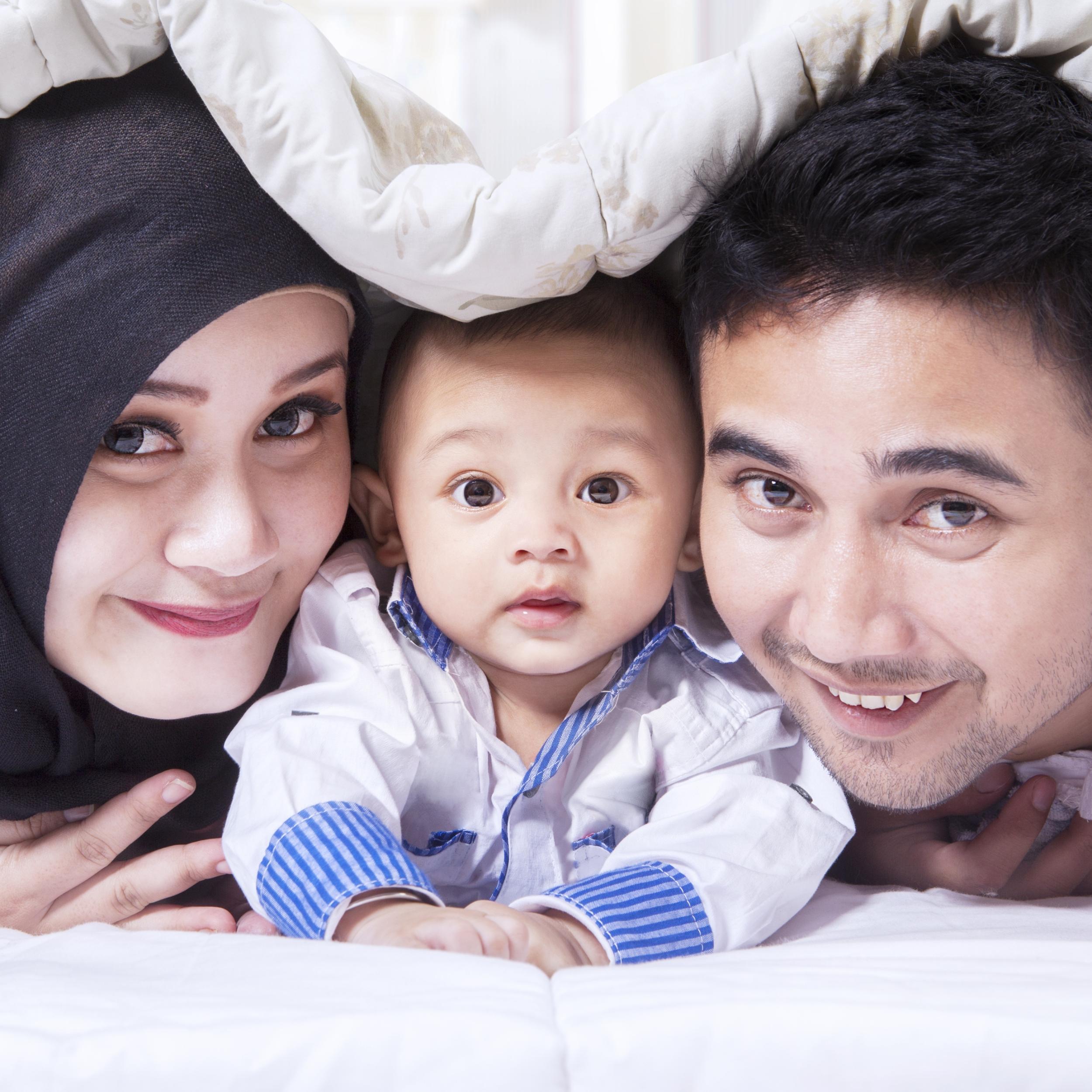 Familienbild mit einer jungen Mutter mit Kopftuch, einem Baby in der Mitte und einem Vater