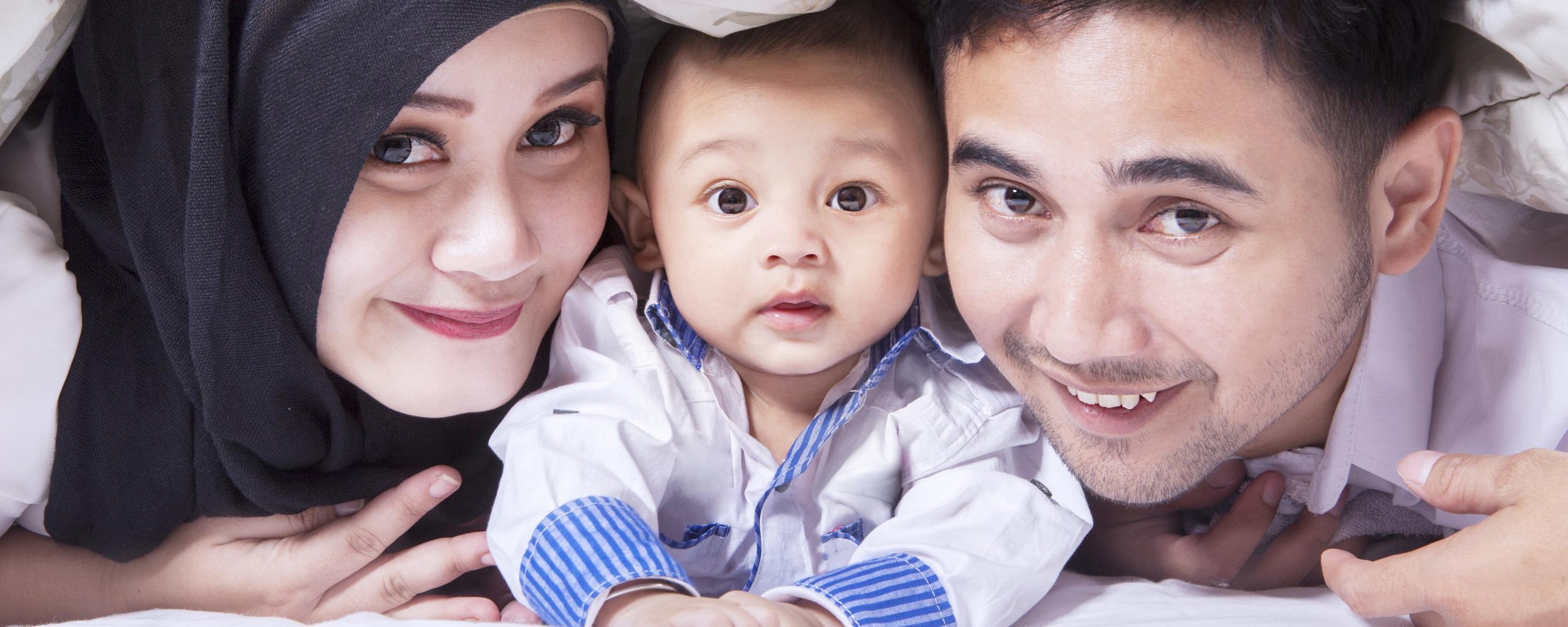Familienbild mit einer jungen Mutter mit Kopftuch, einem Baby in der Mitte und einem Vater