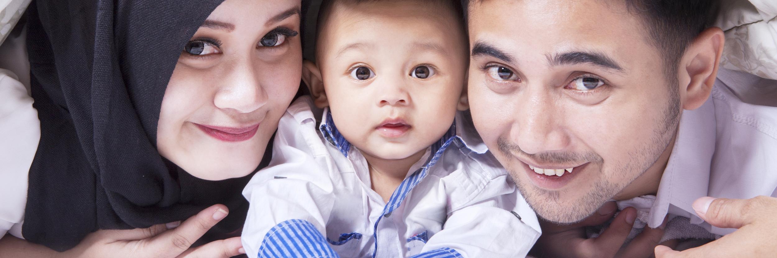 Familienbild mit einer jungen Mutter mit Kopftuch, einem Baby in der Mitte und einem Vater