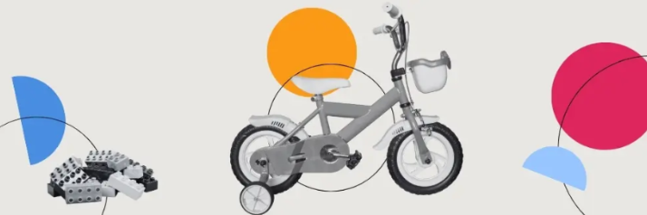 Bausteine und Kinderfahrrad mit Stützrädern auf beigem Untergrund umgeben von bunten (Halb-)Kreisen