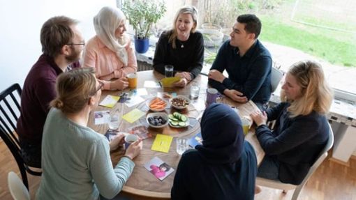 Sieben Menschen sitzen um einen runden Tisch und unterhalten sich