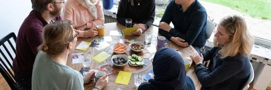 Sieben Menschen sitzen um einen runden Tisch und unterhalten sich
