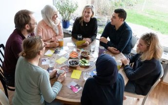 Sieben Menschen sitzen um einen runden Tisch und unterhalten sich