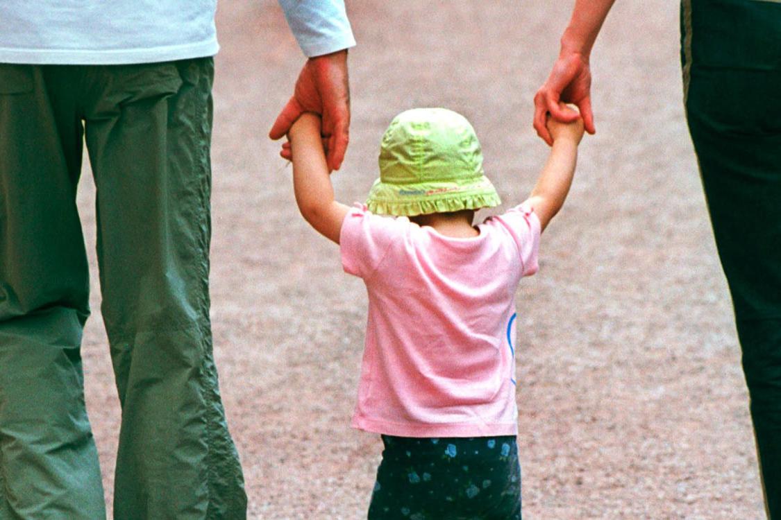Eltern, die ein Kind zwischen sich an den Händen fassen