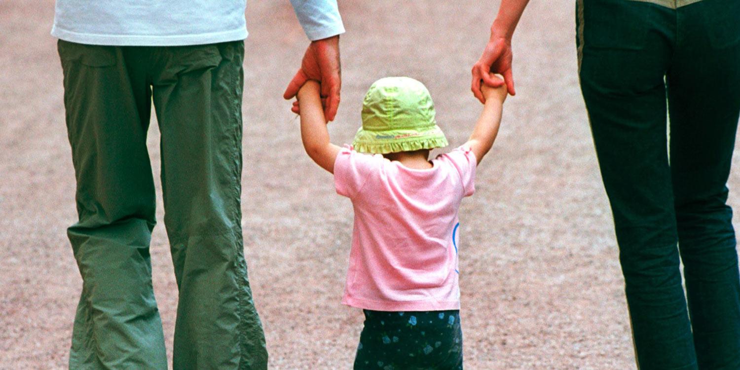 Eltern, die ein Kind zwischen sich an den Händen fassen