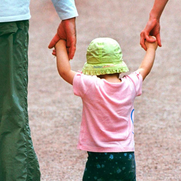 Eltern, die ein Kind zwischen sich an den Händen fassen
