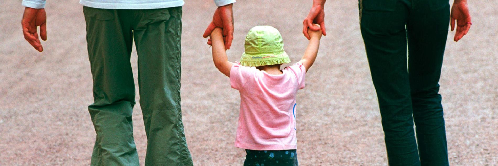Eltern, die ein Kind zwischen sich an den Händen fassen