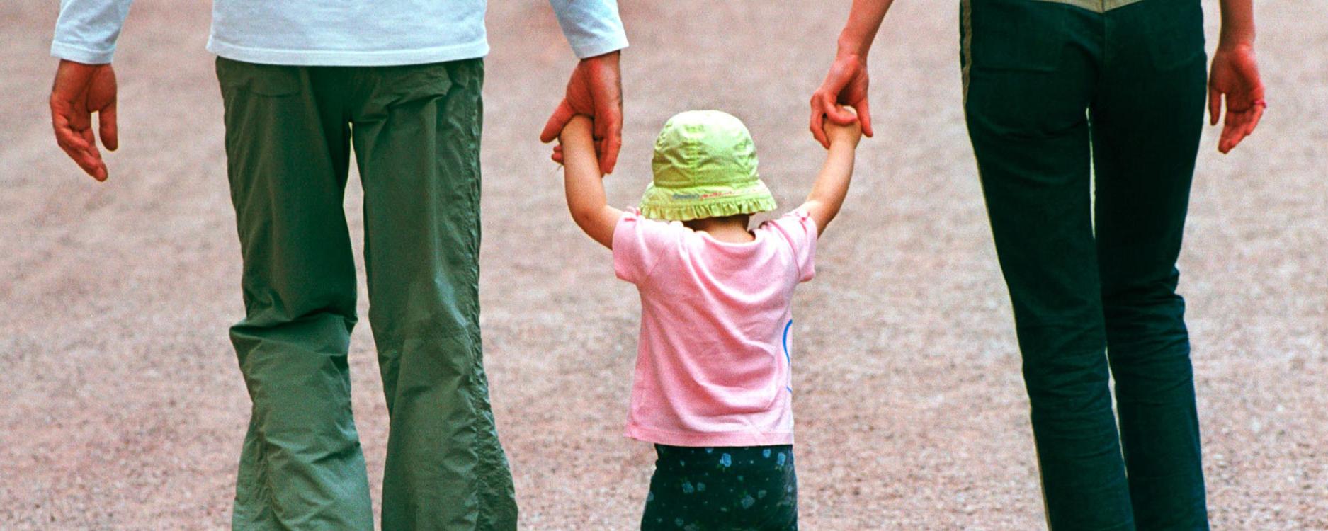 Eltern, die ein Kind zwischen sich an den Händen fassen