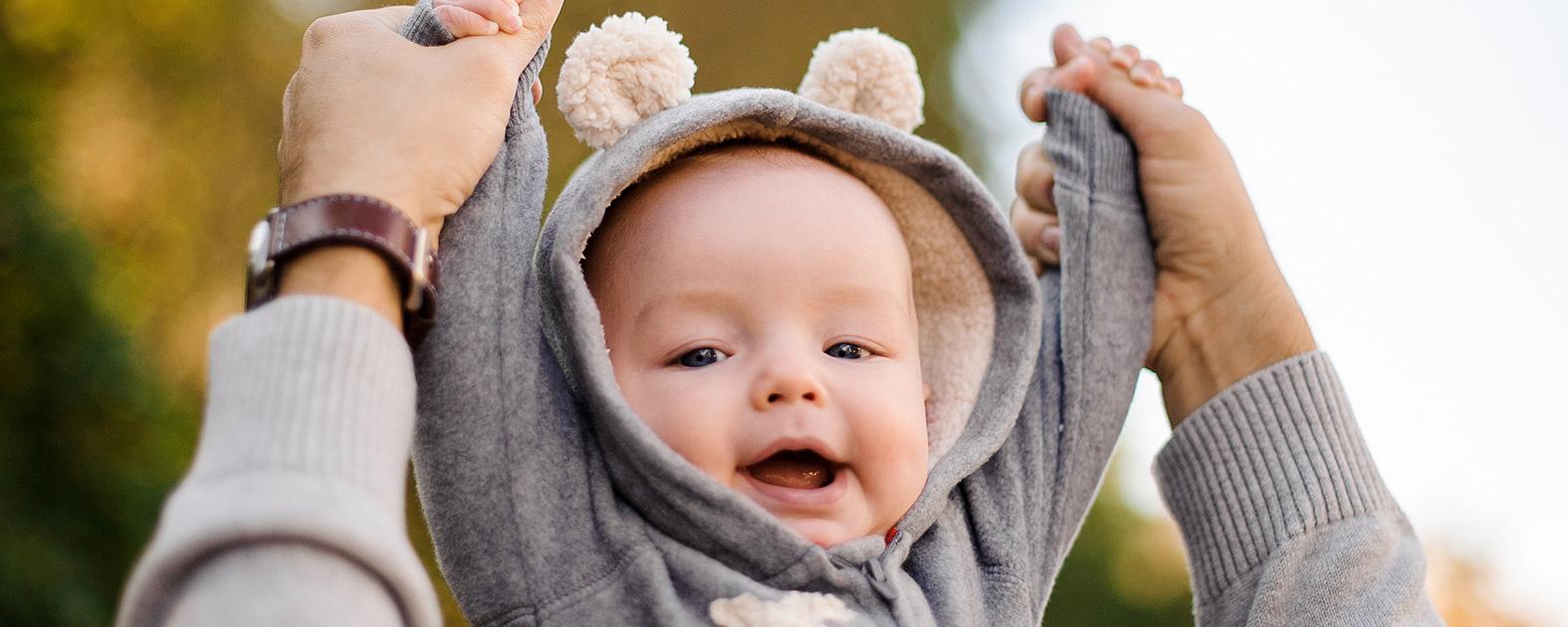 Bild mit lächelndem Baby, das die Arme mit Hilfe eines Elternteils nach oben streckt.