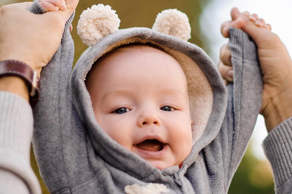 Bild mit lächelndem Baby, das die Arme mit Hilfe eines Elternteils nach oben streckt.