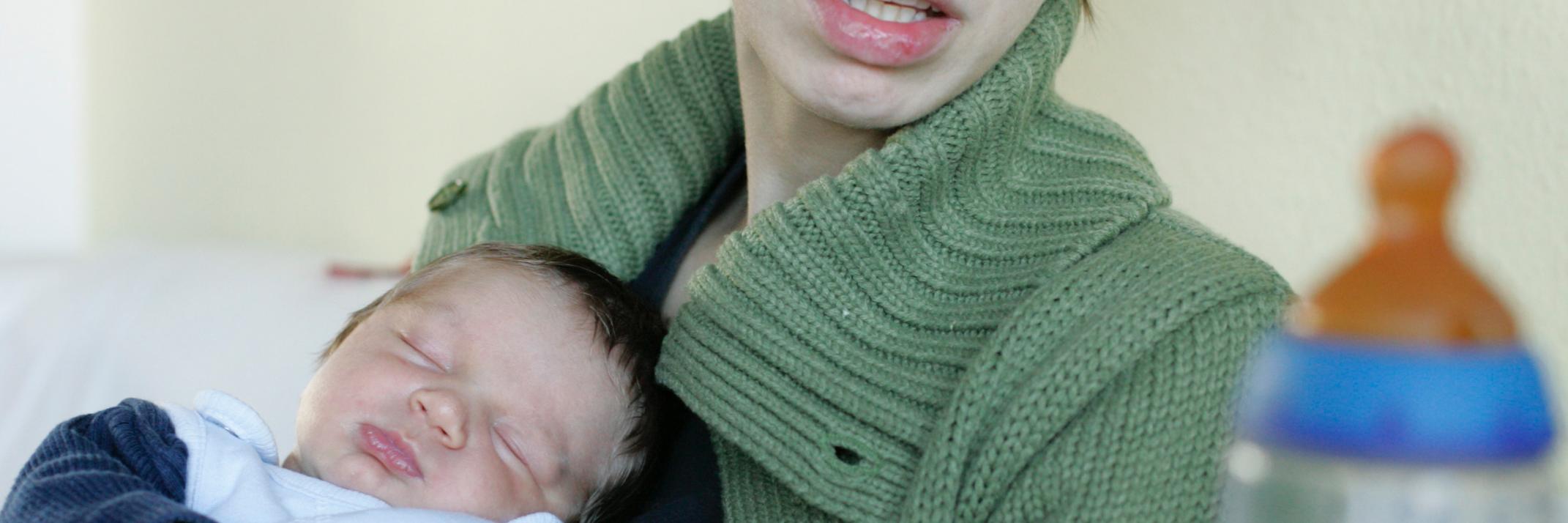 Mutter mit schlafendem Baby auf dem Arm, die überfordert aussieht