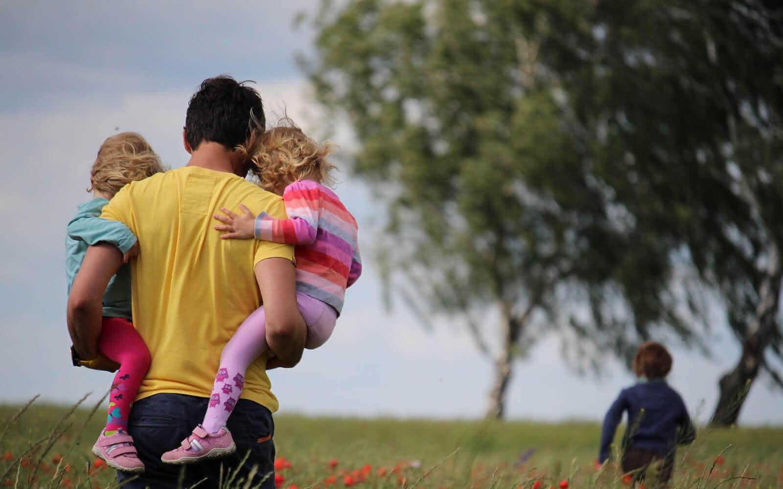 Mann der zwei Kinder in einer Wiese trägt