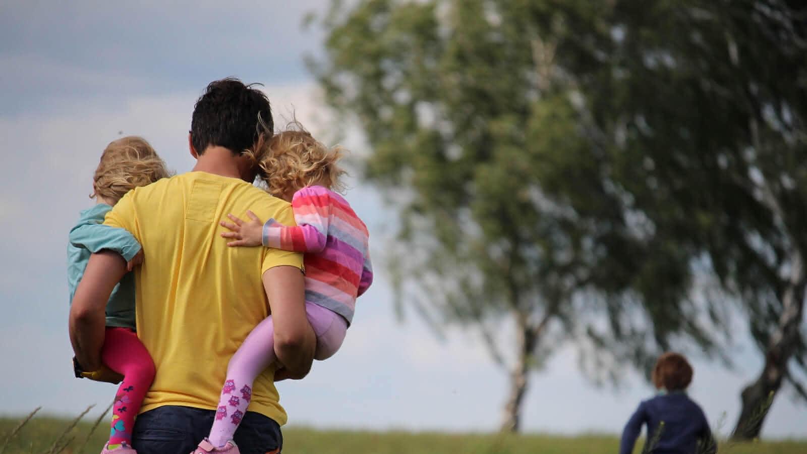 Mann der zwei Kinder in einer Wiese trägt