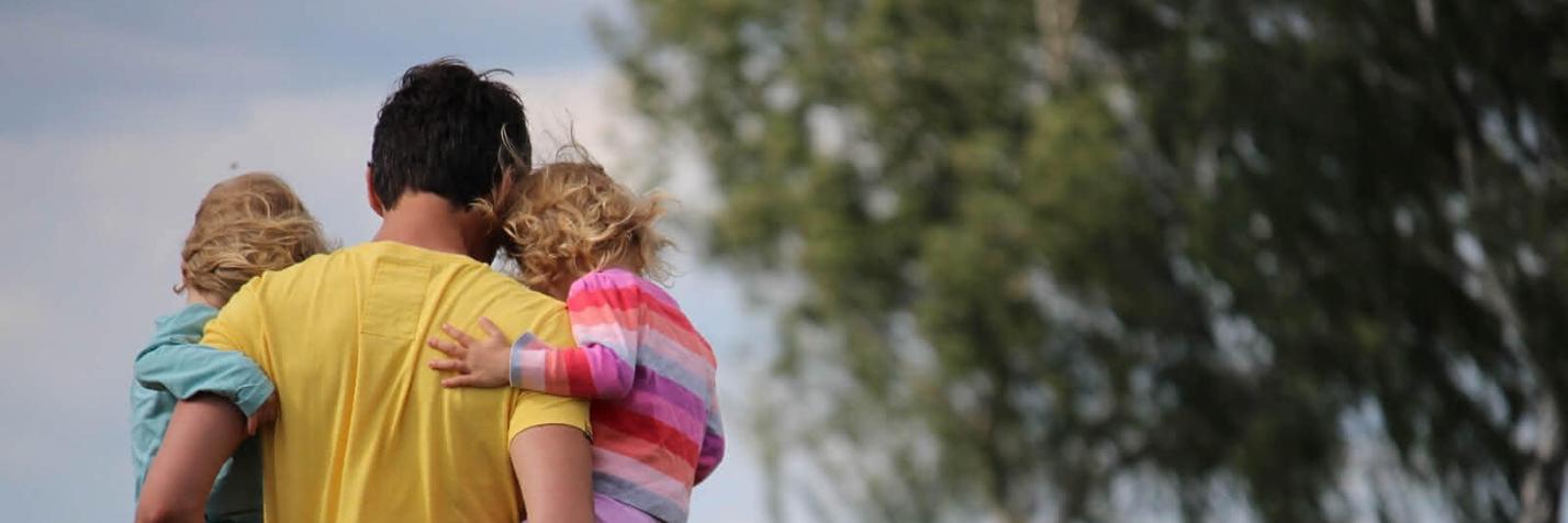 Mann der zwei Kinder in einer Wiese trägt